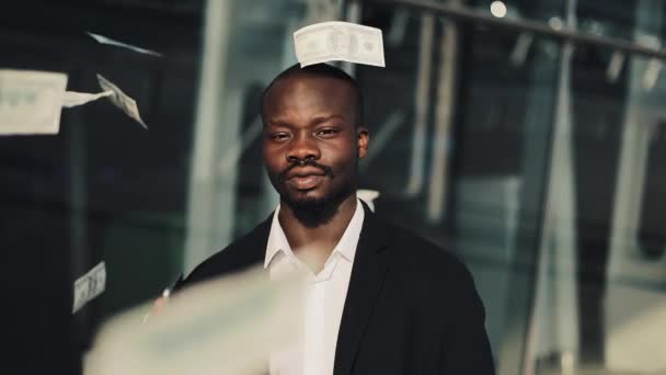 Retrato de um empresário afro-americano a olhar para a câmara enquanto o dinheiro voa por todo o lado. Ele tem o smartphone nas mãos. Chuva de dinheiro sobre o empresário em câmera lenta — Vídeo de Stock