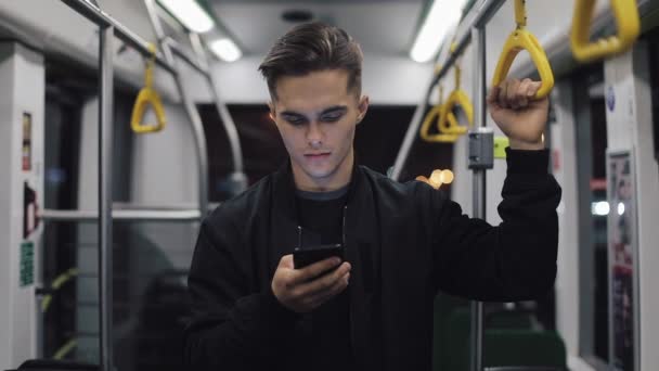Vonzó férfi portréja tartja a kapaszkodó segítségével állandó smartphone, a tömegközlekedésben. Város lámpák háttér — Stock videók