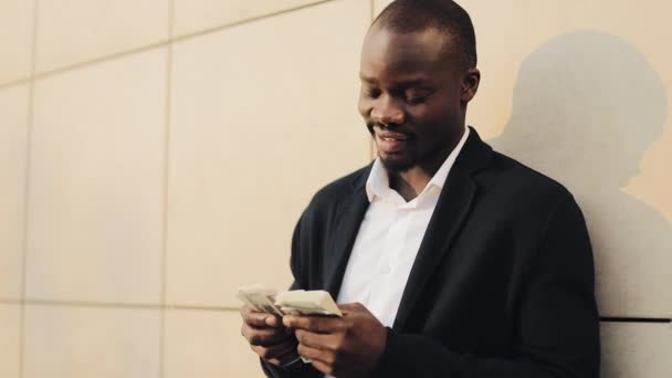 Un homme d'affaires afro-américain en costume comptant de l'argent et montrant de l'argent dans la caméra. Il célèbre sa victoire avec beaucoup de dollars. — Video