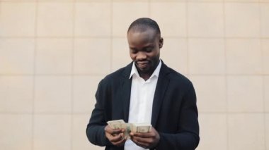 Office merkezine yakın para ayakta sayma takım elbiseli Afrikalı-Amerikalı işadamı portresi. O onun başarılı kazanmak dolar bir çok ile kutluyor ve kameraya bakıyor