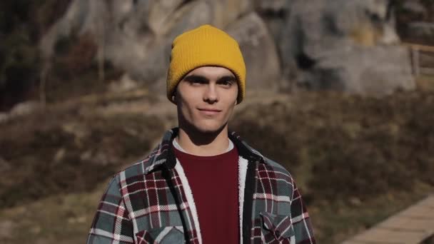 Portré fiatal természetjáró ember állt, a hegyekben, és mosolyog a kamerába. Gyönyörű sziklák háttér. A szabadban — Stock videók
