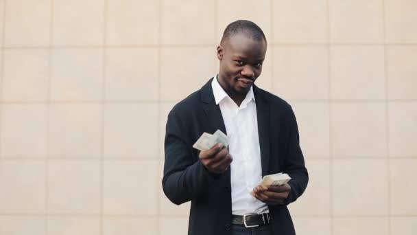Portrait d'un homme d'affaires afro-américain en costume comptant de l'argent debout près du centre de bureau. Il célèbre sa victoire réussie avec beaucoup de dollars et regarde dans la caméra — Video