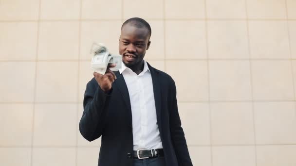 Счастливый африканский американский бизнесмен держит в руках большую сумму денег. Он стоит на улице рядом с офисным центром или банком и показывает деньги на камеру Лицензионные Стоковые Видео