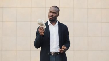 Office merkezine yakın para ayakta sayma takım elbiseli Afrikalı-Amerikalı işadamı portresi. O onun başarılı kazanmak dolar bir çok ile kutluyor ve kameraya bakıyor