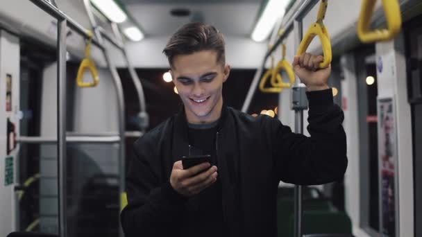 Portret atrakcyjnych mężczyzn posiada poręczy, przy użyciu smartfona stojący w transporcie publicznym. Tle światła miasta — Wideo stockowe