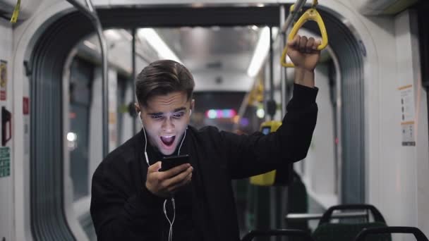 Feliz hombre de negocios animando celebrando mirando el teléfono inteligente. Joven profesional urbano exitoso hombre de negocios recibiendo buenas noticias cabalgando en transporte público. Él sostiene la barandilla — Vídeo de stock