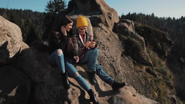 Pareja joven enamorada se sienta en la roca y toma un retrato de selfie. Hombre y mujer visitando la famosa atracción turística — Vídeos de Stock