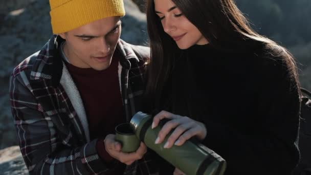 Paar in liefde drinken thee uit een mok thermos op de achtergrond van bergen. Toeristen zittend op stenen en op de prachtige natuur. Toerisme, rust, vakantie, natuur, wandeling concept — Stockvideo