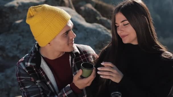 Pareja en el amor beber té de una taza de termo en el fondo de las montañas. Turistas sentados en piedras y mirando la hermosa naturaleza. Turismo, descanso, vacaciones, naturaleza, concepto de caminata — Vídeo de stock