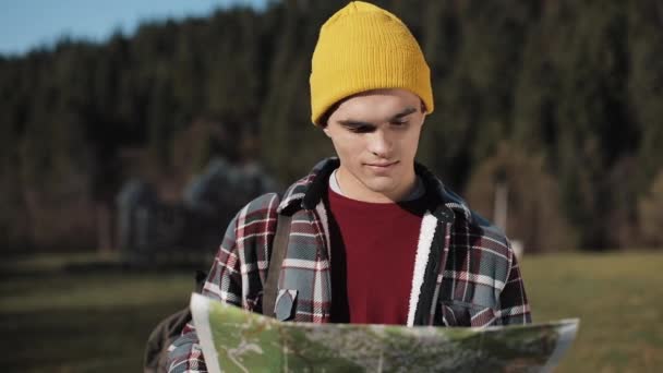 Viajando a las montañas. El excursionista sostiene el viejo mapa de pie en el bosque y mirando a su alrededor. El turista viaja en hermosas montañas — Vídeos de Stock