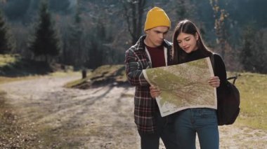 Mutlu çift ayakta dağlarda gülümseyen genç. Onlar onların yürüyüş zevk almak. Turistik harita üzerinde seyir. Yön bulmaya çalışıyorum. Ağır çekim