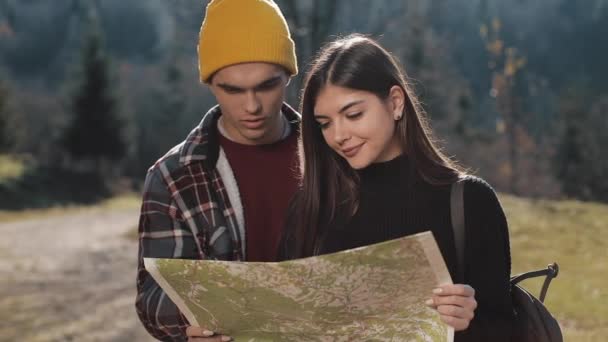 Pasangan muda tersenyum bahagia berdiri di pegunungan. Mereka menikmati hiking mereka. Melihat peta turis. Mencoba untuk menemukan arah. Pergerakan Lambat — Stok Video