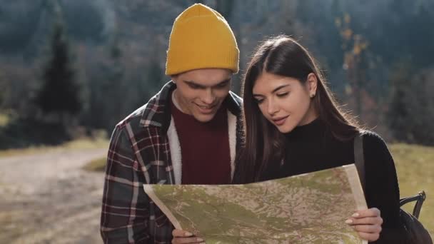 Молода усміхнена щаслива пара, що стоїть у горах. Вони насолоджуються пішохідним туризмом. Дивлячись на туристичну карту. Спроба знайти напрямок. Повільний рух — стокове відео