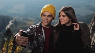 Genç aşk oturur yüksek dağda bir kayanın üzerinde çift ve selfie telefonda yapmak. Ağır çekim