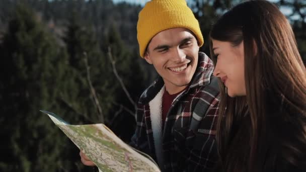Viaja a las montañas. Hermosa pareja enamorada se sienta en la roca y aprende un mapa. Hablan entre ellos, se ríen y se divierten — Vídeo de stock