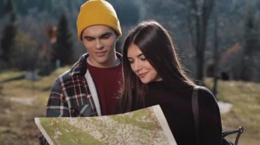 Mutlu çift ayakta dağlarda gülümseyen genç. Onlar onların yürüyüş zevk almak. Turistik harita üzerinde seyir. Yön bulmaya çalışıyorum. Ağır çekim