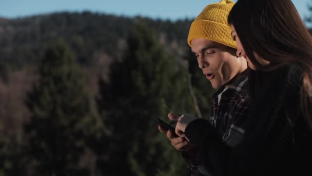 Cestovat na horách. Nádherný pár v lásce sedí na skále a smartphone. Muž ukazuje přítelkyni něco na svém telefonu — Stock video