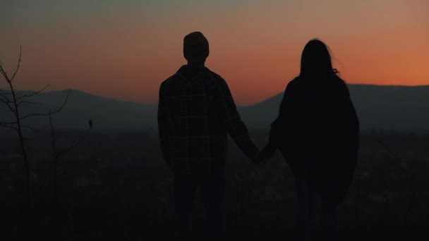 Silueta de pareja joven enamorada disfrutando de una puesta de sol sobre las montañas. Vacaciones, viajes, romance, concepto de propuesta de matrimonio — Vídeo de stock