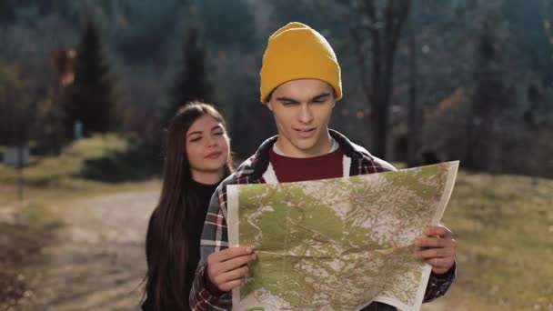 Joven pareja feliz sonriente de pie en las montañas. Disfrutan de su caminata. Buscando en el mapa turístico. Tratando de encontrar la dirección. Moción lenta — Vídeos de Stock