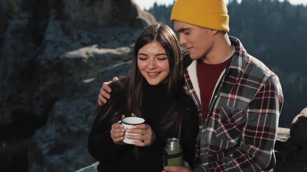 Verliebte Paare trinken Tee aus einem Becher Thermoskanne vor dem Hintergrund der Berge. Touristen sitzen auf Steinen und schauen auf die schöne Natur. Tourismus, Erholung, Urlaub, Natur, Wanderkonzept — Stockvideo