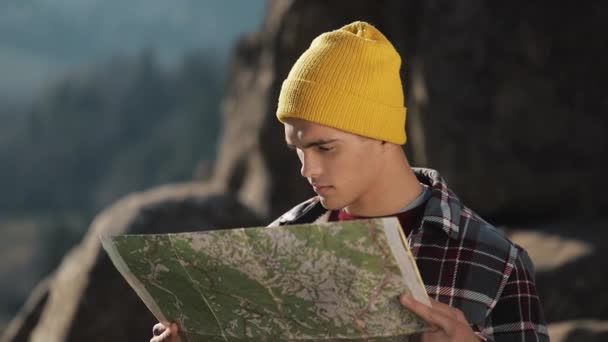 Viajando a las montañas. El excursionista sostiene el viejo mapa de pie en la cima de la roca. El turista viaja en hermosas montañas — Vídeos de Stock