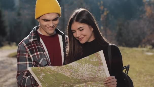 Pasangan muda tersenyum bahagia berdiri di pegunungan. Mereka menikmati hiking mereka. Melihat peta turis. Mencoba untuk menemukan arah. Pergerakan Lambat — Stok Video