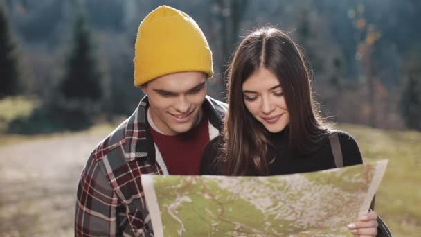 年轻的微笑幸福的夫妇站在山上。他们喜欢徒步旅行。查看旅游地图。试图找到方向。慢动作 — 图库视频影像