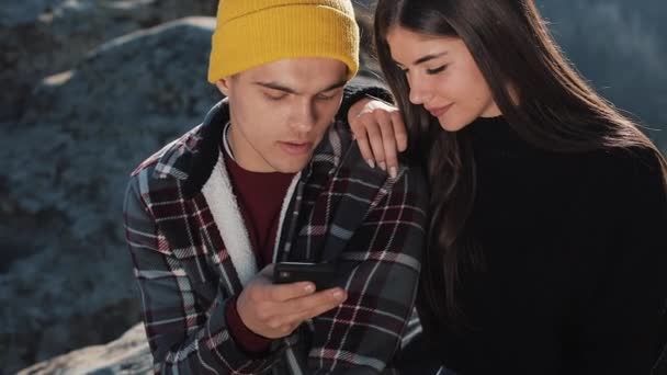 Cestovat na horách. Nádherný pár v lásce sedí na skále a použití mapy na smartphone. Muž ukazuje přítelkyni něco na svém telefonu. — Stock video