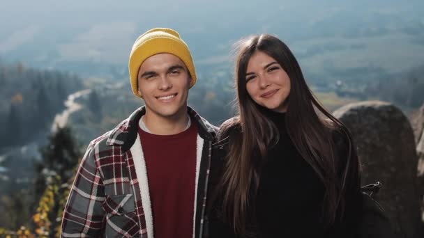 Pareja de jóvenes turistas felices se encuentra en las rocas en las hermosas montañas. Miran a la cámara y sonríen — Vídeos de Stock