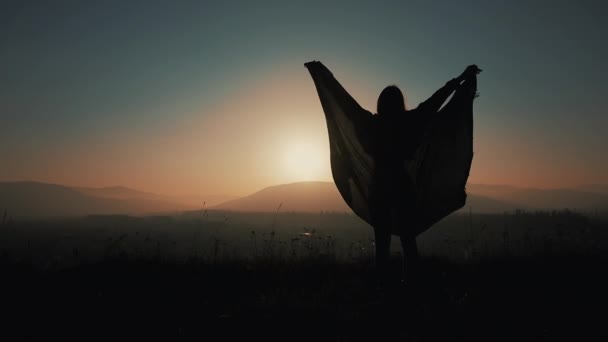 Silhouette di una bella donna con pareo che raggiunge la cima della montagna, alza le mani e guarda il paesaggio — Video Stock