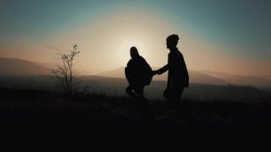 Birkaç aşk dağlarda silüeti. Yürüyüşçüler erkek ve kadın çalışan trekking günbatımında dağlarda eşleyin. Onlar el ele tutuşarak