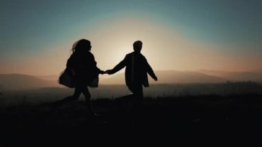 Birkaç aşk dağlarda silüeti. Yürüyüşçüler erkek ve kadın çalışan trekking günbatımında dağlarda eşleyin. Onlar el ele tutuşarak