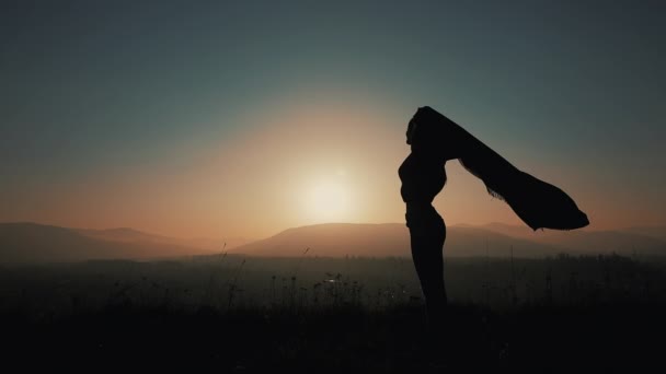 Silhouette einer schönen jungen Frau, die mit einem Pareo in der Hand durch die Berge läuft. Zeitlupe. das Konzept der Freiheit, Leichtigkeit, Erfolg, Ruhe. Sonnenuntergang — Stockvideo