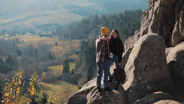 恋爱中的年轻夫妇站在岩石上, 拍了一张自拍的肖像。男子和妇女参观著名的旅游景点 — 图库视频影像