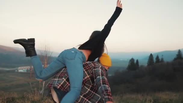 Young couple in love on vacations enjoying mountains. Attractive man is carrying girlfriend on his shoulders and whirls her. Having fun — Stock Video