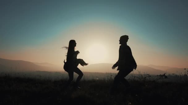 Una pareja amorosa corre para encontrarse en abrazo, el hombre retuerce a su mujer contra la puesta de sol en las montañas. Cámara lenta, silueta — Vídeos de Stock