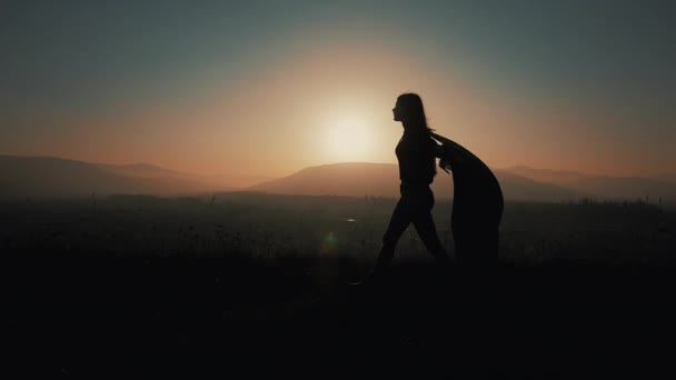 Siluet seorang wanita muda yang cantik berjalan di pegunungan dengan pareo di tangannya. Gerakan lambat. Konsep kebebasan, kemudahan, keberhasilan, istirahat. Matahari terbenam — Stok Video