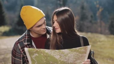 Mutlu çift ayakta dağlarda gülümseyen genç. Onlar onların yürüyüş zevk almak. Turistik harita üzerinde seyir. Yön bulmaya çalışıyorum. Ağır çekim