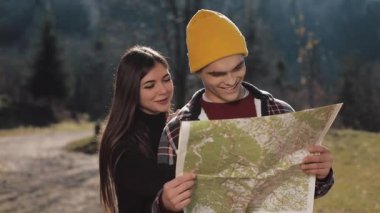 Mutlu çift ayakta dağlarda gülümseyen genç. Onlar onların yürüyüş zevk almak. Turistik harita üzerinde seyir. Yön bulmaya çalışıyorum. Ağır çekim