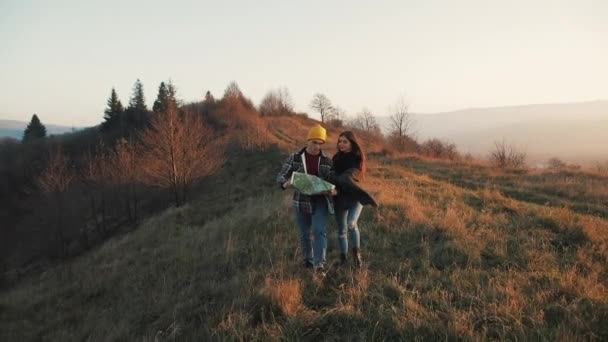 Paar verliefd buiten wandelen. Wandelaars man en vrouw trekking wandelen met rugzakken in parcours met kaart bij zonsondergang in Bergen — Stockvideo