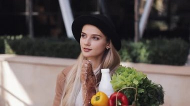 Genç güzel kadın bir paket gülümseyen ve etrafa ürünlerin holding sokakta yürürken şık bir palto giyiyor. Alışveriş, sağlıklı beslenme