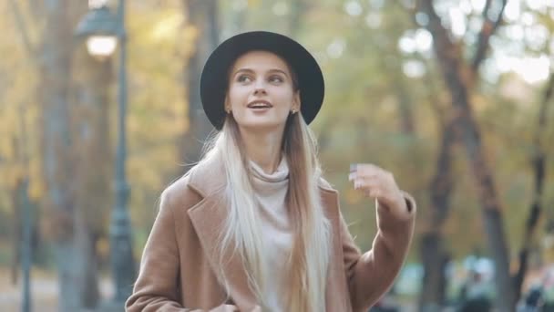 Fille incroyable dans un look romantique, avec chapeau noir marchant dans l'allée du parc, regardant autour et donne un sourire incroyable. Cadre du parc, arbres, feuilles tombées sur le fond — Video