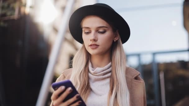 Όμορφη ελκυστική γυναίκα που φοράει παλτό και καπέλο μιλάει μέσω τηλεφώνου στο κέντρο της πόλης σε μια ηλιόλουστη Άνοιξη καιρού — Αρχείο Βίντεο