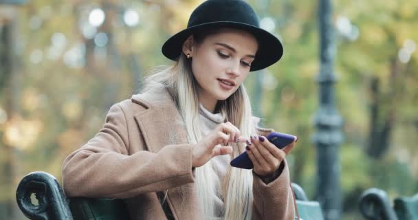 Ευτυχισμένη γυναίκα χρησιμοποιώντας μια λειτουργία αναγνώρισης φωνής του smartphone. Αυτή κάθεται σε παγκάκι στο φθινόπωρο πάρκο και υπαγορεύει τις σκέψεις, το μήνυμα κλήσης φωνής — Αρχείο Βίντεο