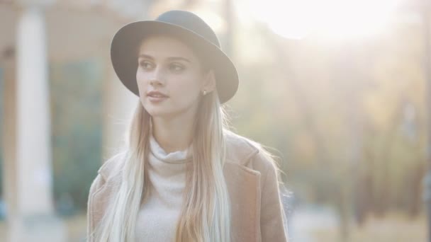 Şaşırtıcı kız romantik siyah şapkalı park sokakta yürürken etrafa bak ve şaşırtıcı gülümseme verir. Park ayarları, ağaçlar, arka plan üzerine düşen yapraklar — Stok video