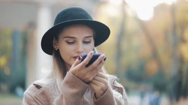 Företag dam i svart hatt skicka ljud röstmeddelande på mobiltelefon på utomhus talar till mobila assistent. Flicka med smartphone röstigenkänning, dikterar tankar, uppringning röstmeddelande — Stockvideo