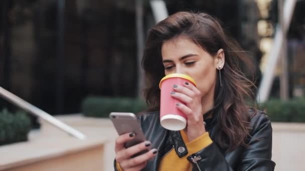 Joven mujer feliz usando teléfono inteligente y beber café para salir al aire libre, caminando por la calle de la ciudad, cámara lenta — Vídeos de Stock