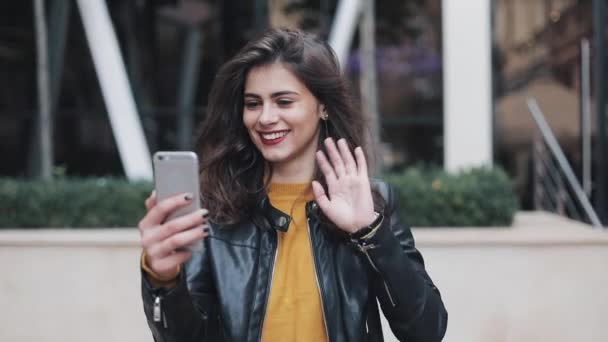 Portrét šťastné mladé ženy mluví o video volání na telefonu stojící poblíž budovy na ulici — Stock video