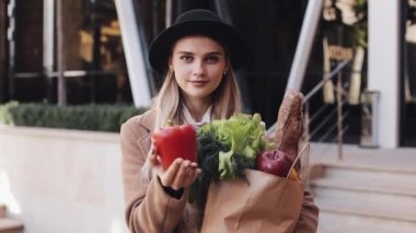 Sokakta bir paket gülümseyen ve kameraya bakarak ürünlerin tutan şık ceket ayakta giyen genç güzel kadın. O kırmızı biber elinde tutar. Alışveriş, sağlıklı beslenme