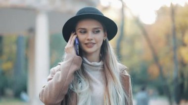 Palto ve şapka giyen güzel çekici kadın bir güneşli bahar hava şehir merkezinde telefonla konuşuyor